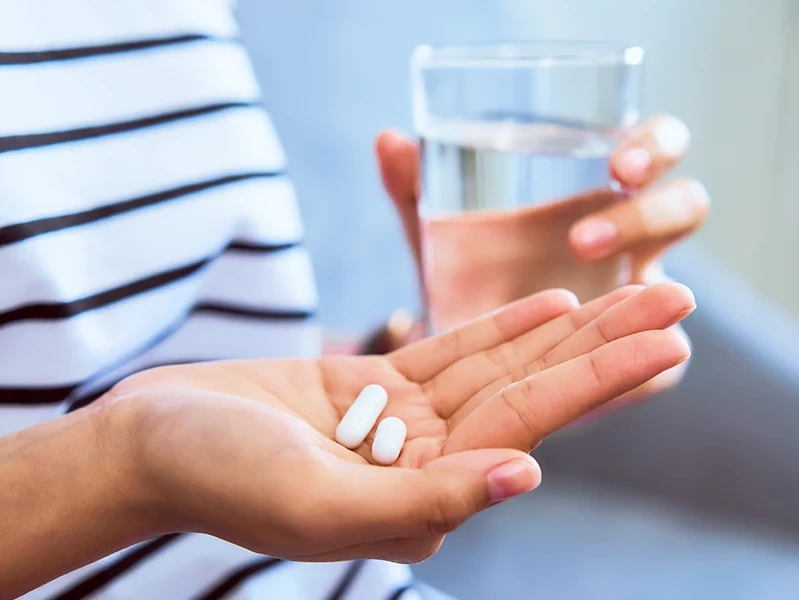 Frau hält Tabletten und ein Glas Wasser in ihren Händen